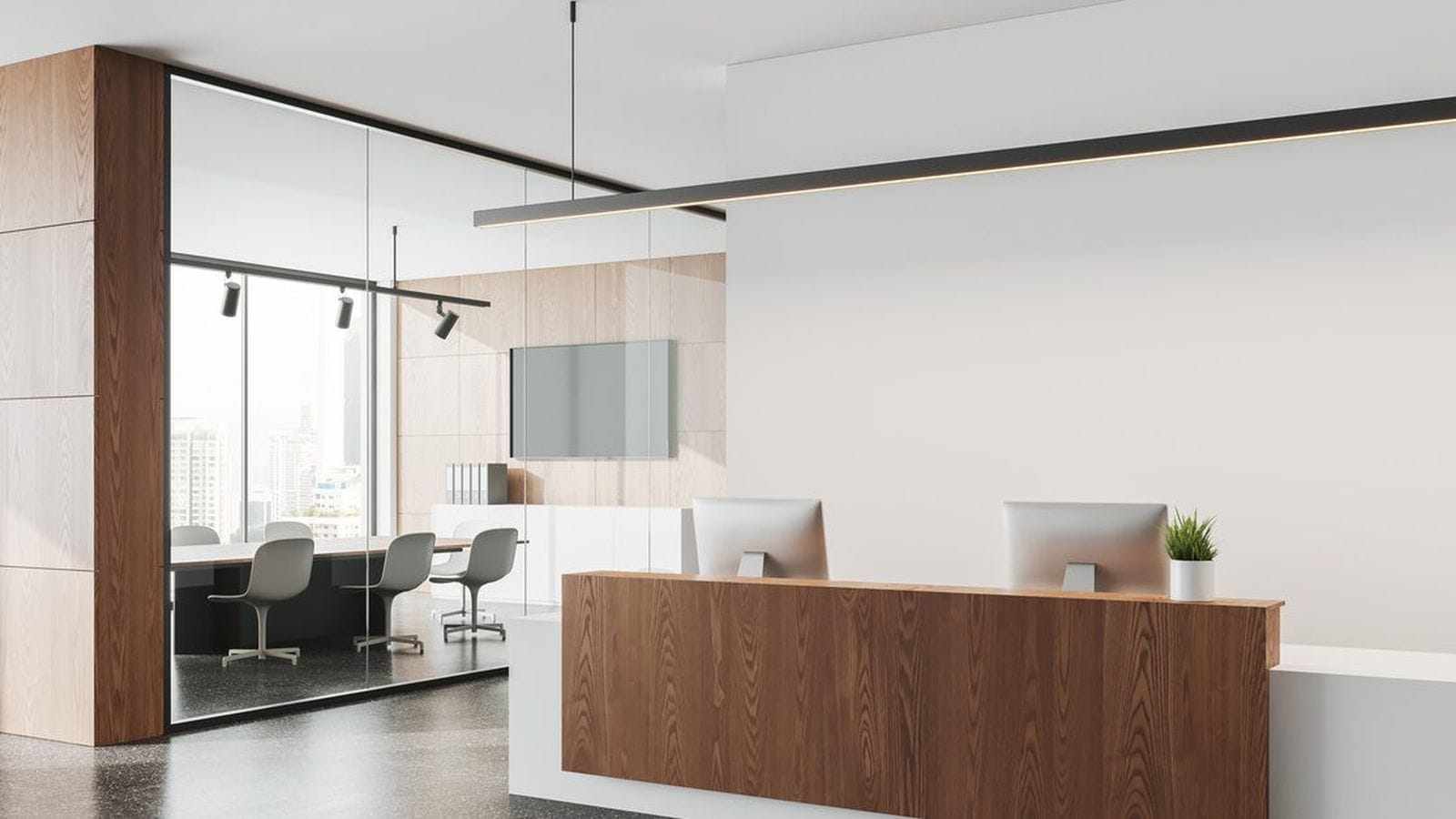 Modern wood-finish reception desk with dual monitors in a bright office lobby